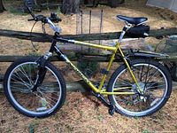 Side view of gold Norton Scrambler mountain bike showing aluminum frame, SR Suntour front suspension fork, V-brakes, rear rack and saddle bag