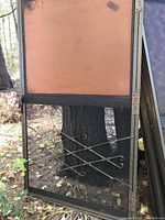 Screened panel with metal frame featuring orange privacy screen and black mesh, some visible damage and outdoor setting.