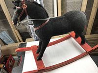 Full side view of vintage black rocking horse on red wooden rockers in basement setting
