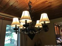 Overall view of the five-arm chandelier with lit beige fabric shades hanging from ceiling.