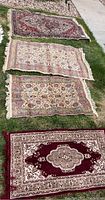 Four rectangular prayer rugs laid out on grass showing overall patterns and colors