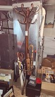 Full view of an antique wooden coat rack with umbrella holder ring at base, showing several umbrellas inside and wooden coat hooks on the top section.