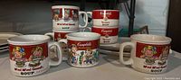 Nine ceramic pieces including mugs and shallow trays with Campbell's Soup graphics and text.