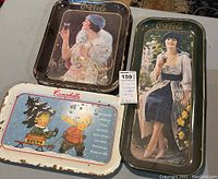 Three vintage advertising trays arranged on a table showing all items in lot.