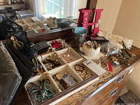 Wide view showing multiple compartments with assorted costume jewelry, beads, and chains on a wooden dresser.