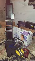 Full view of black vertical media tower filled with CDs, cardboard boxes, and other media items on the floor near a rug.