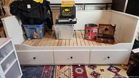 White wooden twin daybed with three drawers beneath and a clutter of objects on top of the bed platform.