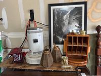 Wide view of lot showing lanterns, heater, Ansel Adams print, wooden cubby organizer with brass figurines and tin on top, brass bull figure and wooden duck figurines