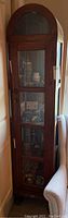Front view of curved wooden cabinet with four glass panels. Key lock visible on lower section. Cabinet contains various display items not included in sale.