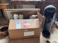 Photo of Nespresso coffee machine, alabaster goblets, desk bed tray and sealed cardboard box on carpet.