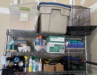 View of three metal shelves with various bins, bottles, bird cage, and supplies organized.