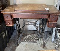Full front view of vintage Singer treadle sewing machine cabinet showing wood tabletop, drawers and metal treadle base with 'SINGER' stamped.