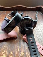 Two smartwatches and four interchangeable bands arranged on wooden surface, round watch on charging dock visible.