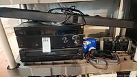 Photo showing Sony AV receiver, Magnavox CD changer, blue Polaroid 300 camera, soundbar speaker, and cables on gray shelving.