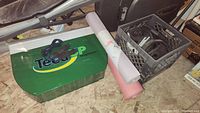 View of the golf swing trainer, yoga mats, and plastic crate with weight plates on the floor.