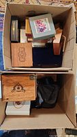 View of two cardboard boxes containing multiple wooden and decorative vintage boxes, some with unique lid designs and various sizes.