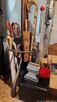 Photo showing a Dremel shoe polisher with red and black cloth pads, multiple umbrellas and canes with wooden handles arranged in a metal umbrella stand.