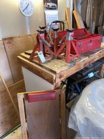 Four red metal car stands, red toolbox, wooden car crawler and assorted tools shown on a workbench in garage environment.