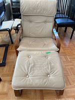 Front view of IKEA Poang armchair with beige leather seat and back cushions and matching ottoman in front, wooden armrests visible.