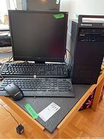 Photo showing Lenovo ThinkCentre desktop computer tower standing next to 19-inch flat panel monitor with two keyboards and a wired Lenovo mouse on a table.