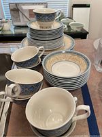 Photo showing stacks of plates, bowls, saucers, and several teacups arranged on a table with blue and cream decorative pattern on dishware
