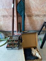 Fishing rods standing vertically behind a metal tackle box with fishing lures inside and an open box containing the Kamik boots.