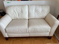 Front view of white leather loveseat with button tufted back cushions, showing overall condition and style