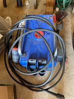 Top view of blue Coleman pressure washer showing hose coiled on top and red button on housing.