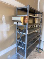Full view of grey metal shelving unit with six shelves and attached stainless steel bin to the side, with wooden mounting block.