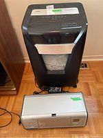 Staples Professional shredder and HP Photosmart printer shown together on wood floor with power cables visible.