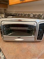 Front view of Oster toaster oven showing stainless steel door, glass window, and digital control panel with multiple settings on right side.