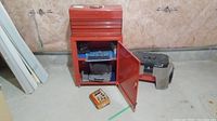Red metal tool box cabinet with door open showing contents including organized tool sets and blocks inside, situated in unfinished basement