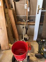 Weed trimmer with handlebar, jerry can, and part of spreader visible in garage.