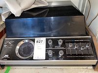 Front view of JVC turntable showing AM/FM tuning dial, control knobs for volume, tuning, balance, and equalizer sliders beneath the dust cover.