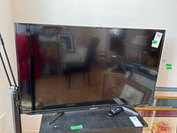 Full front view of the 42 inch Sharp Roku TV on a stand with the remote placed beside it.