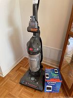 Full view of Hoover WindTunnel upright vacuum and Pelonis ceramic heater in box side by side on floor.