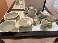 Full assortment of Wedgwood china pieces displayed on mirrored surface showing coffee pot, gravy boat, creamers, bowls, covered dish, and plates.