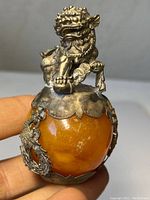 Close-up showing silver Foo Dog figurine seated on an amber sphere with silver embellishments.