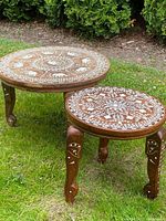 Photo of both nesting tables outdoors showing round tops with white elephant and floral inlay on dark hardwood.