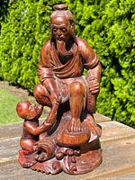 Front and left side angle of the hardwood figure showing the fisherman seated with child, fish, and carved wave base details.