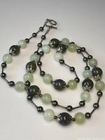 Overall view of antique carved jade 2 tone beaded necklace laid out showing various beads and sterling silver clasp.