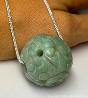 Close-up image of the carved jade bead on the silver necklace showing detailed floral and abstract carvings on the spherical bead.