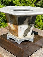 Angled front view showing hexagonal shape, varied natural stone colors, and visible calligraphy on side panels.