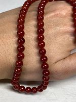 Close-up showing the round cherry amber style beads and glossy finish of the necklace draped over hand.