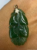 Front view of spinach jade pendant carved in leaf design with gold bail attachment shown on hand for size reference.