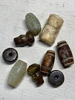 Top view of 9 antique beads made from jade and stone with different shapes and carvings on a white background