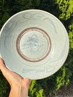 Hand holding the shallow porcelain bowl showing the inside with faint brushstroke decoration and the pale bluish-gray glaze.