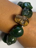 Close-up photo of the bracelet worn on a wrist, showing dark green carved jade skull beads and one tigers eye carved skull bead.