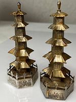 Front angle view of the pair of antique silver pagoda salt and pepper shakers showing their detailed multi-tiered roofs and hexagonal bases with decorative fences.
