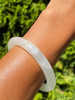 Stone bangle bracelet worn on wrist showing translucency and smooth rounded shape.